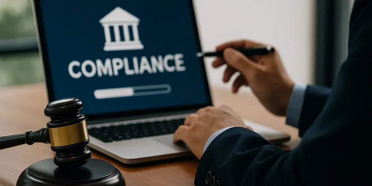 Person in Anzug arbeitet am Laptop mit „Compliance“-Anzeige, neben einem Richterhammer auf dem Tisch.